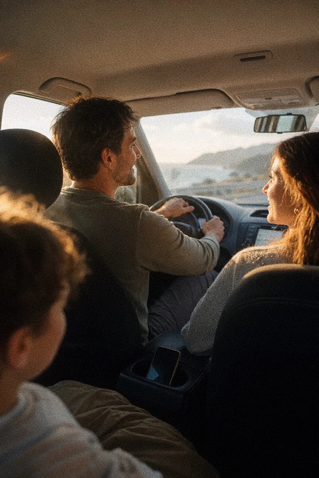 Family driving along a coastal road in warm afternoon light.