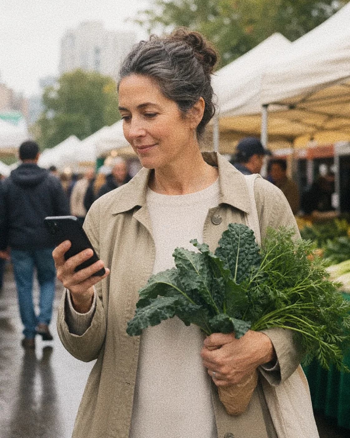 Person at a market holding greens and checking a phone.